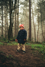 a boy in a coat standing in a forest 