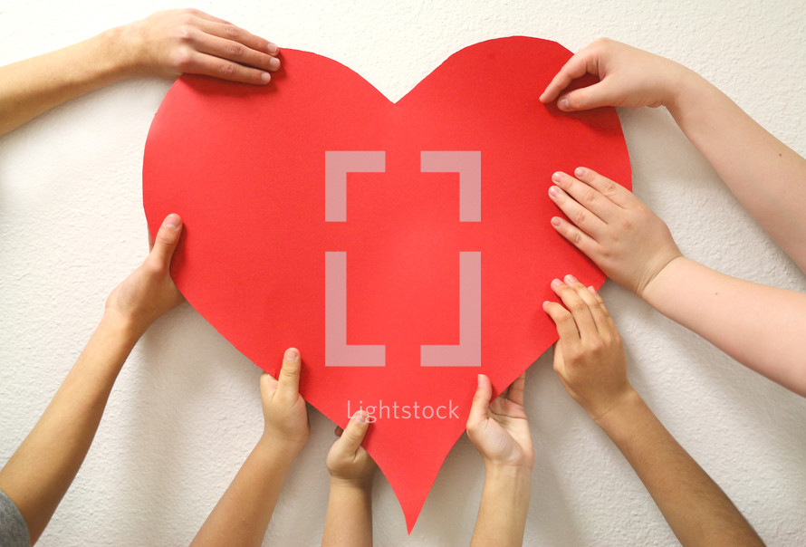 kids hands holding up a red heart 