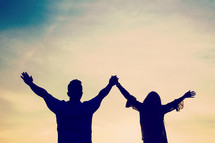 silhouette of a couple together with raised arms outdoors 