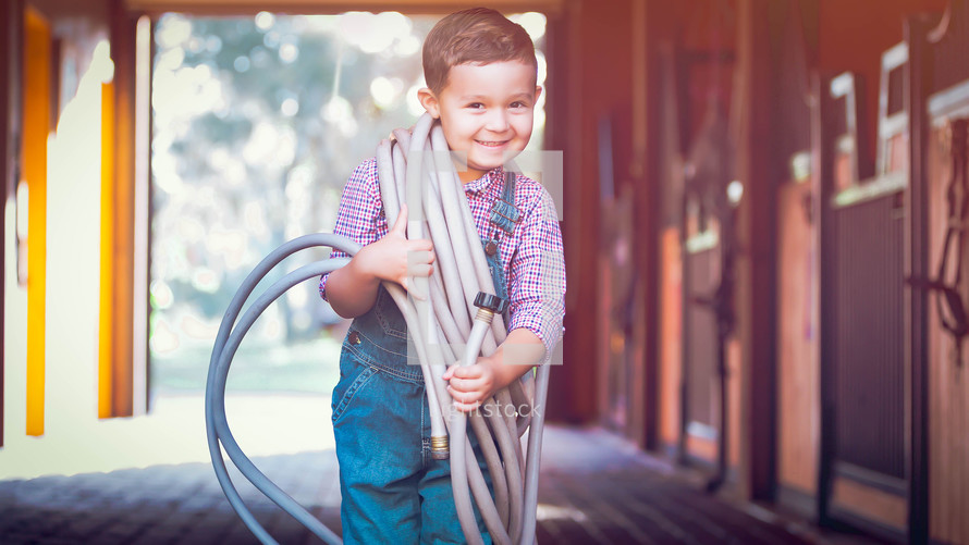 a child holding a hose in a stable 