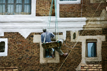 A painter hanging from ropes painting a building in Yemen 