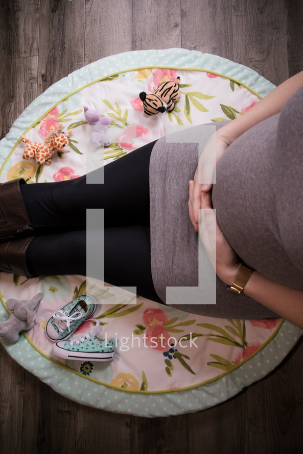pregnant mother sitting on a nursery room rug 