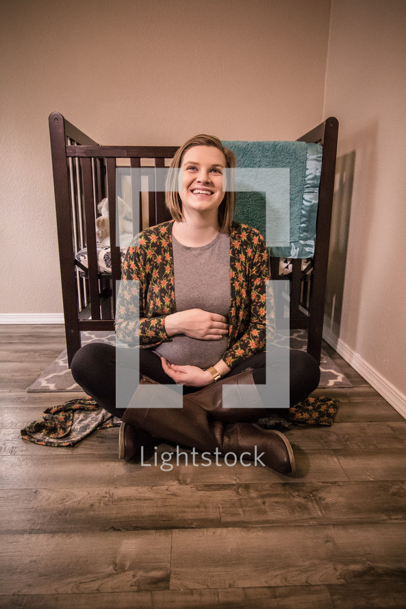 pregnant woman sitting on the floor of a nursery holding her belly 