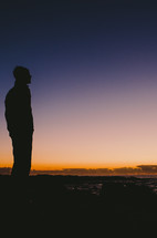 a man looks out over the ocean at dawn