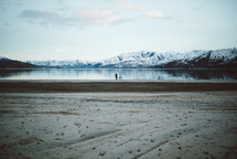a woman standing by a lake surround by snow capped mountains 