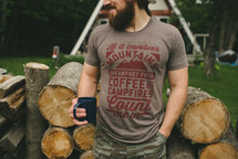 a man drinking coffee next to a stack of logs
