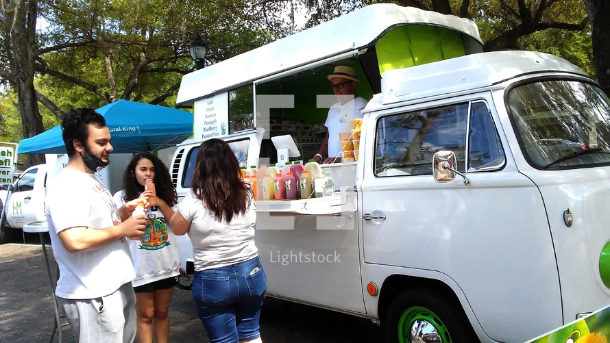 People purchasing food from a local food vendor in a truck at a local outdoor feed festival.