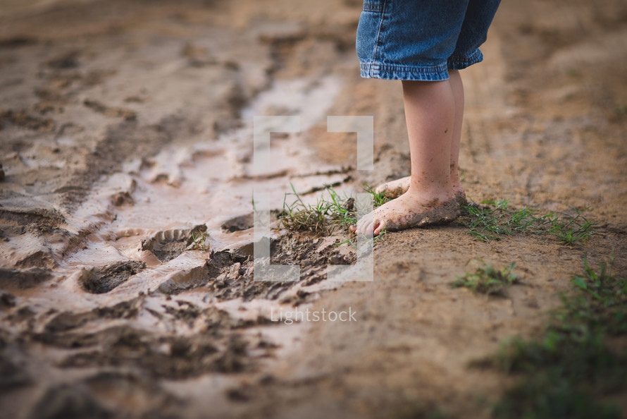 child's bare feet standing in mud 