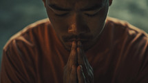 A man praying in an orange shirt with his eyes closed