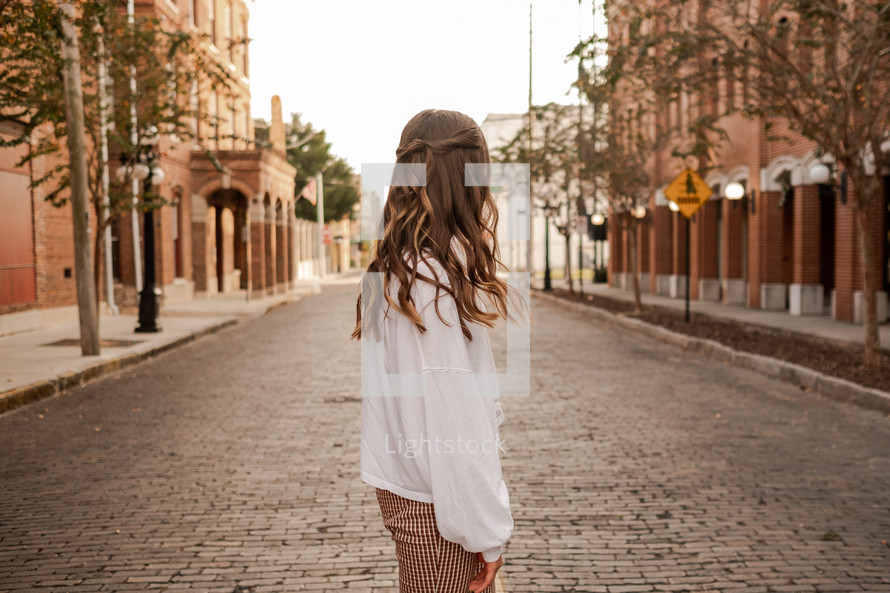 young woman standing in the middle of a cobblestone street 