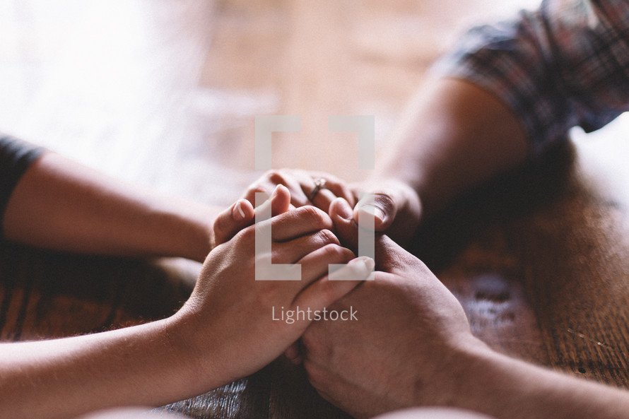 couple holding hands on a wood table 