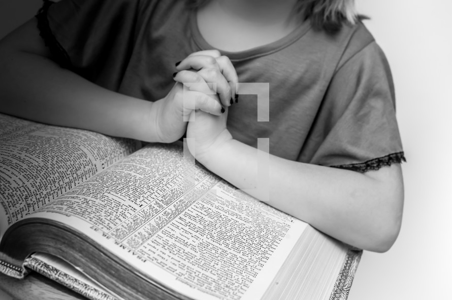 Girl's praying hands resting on an open Bible.