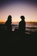 a man and woman look out towards the ocean at dawn
