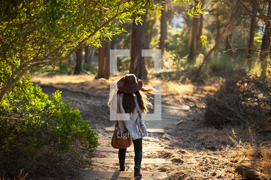 a girl walking on a trail in the woods 