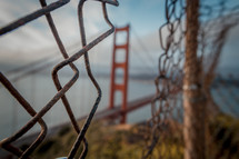 Focus on a hole in a fence in front of Golden Gate Bridge