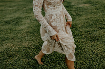 a woman in a lace dress walking through grass