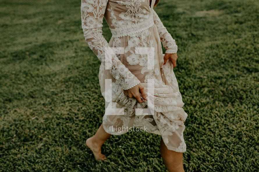 a woman in a lace dress walking through grass