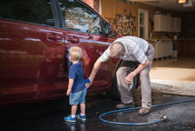 A small boy and his grandfather washing a car together.