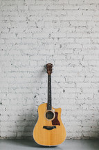 acoustic guitar resting against a brick wall painted white