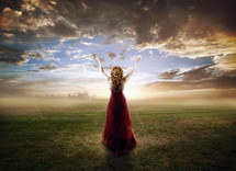 woman in a red gown standing with her arms raised to the sky in worship to God