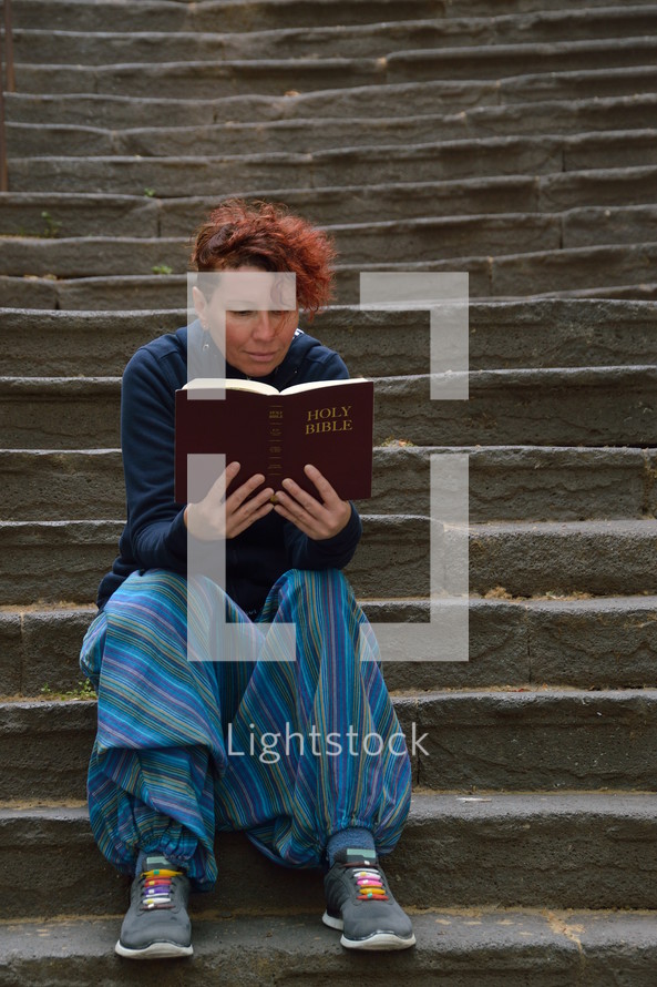 a woman sitting alone on stone steps reading a Bible 