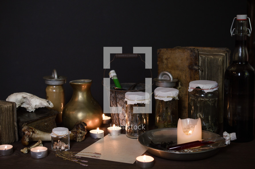 candles in an ancient apocothery  - or:
eerie witches' kitchen with lot of ingredients for a potion and ancient gruesome jars dark with only candlelight for Halloween