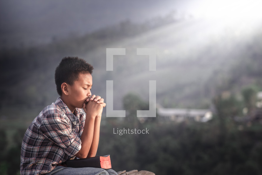 A praying boy sitting outdoors 