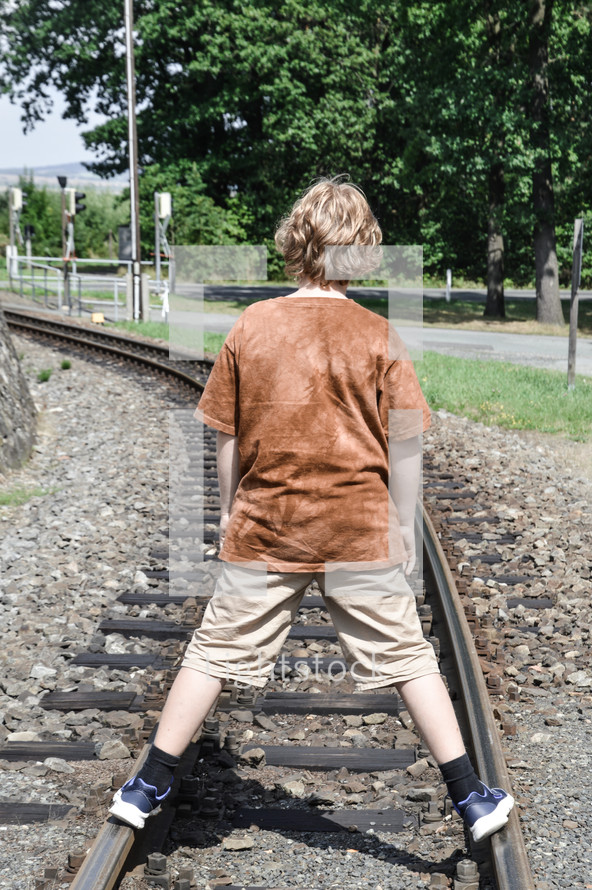 teen boy standing on train tracks 