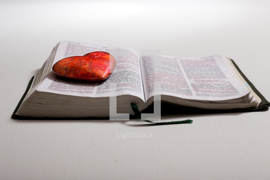 red stone shaped heart stone on pages of a Bible 