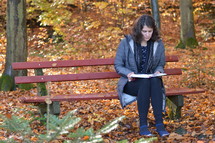 a woman reading on a bench in a park in fall 