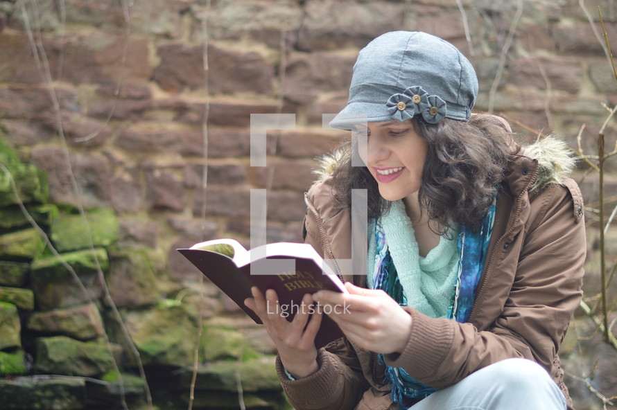 woman reading the bible while sitting outside.
