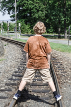 teen boy standing on train tracks 