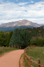 fence lined paved path and mountain peaks 