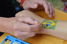 woman painting a brazilian flag on someones arm. 
