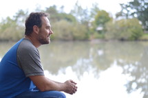 a man sitting by a lake shore thinking 