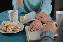 couple holding hands and praying over open Bibles 