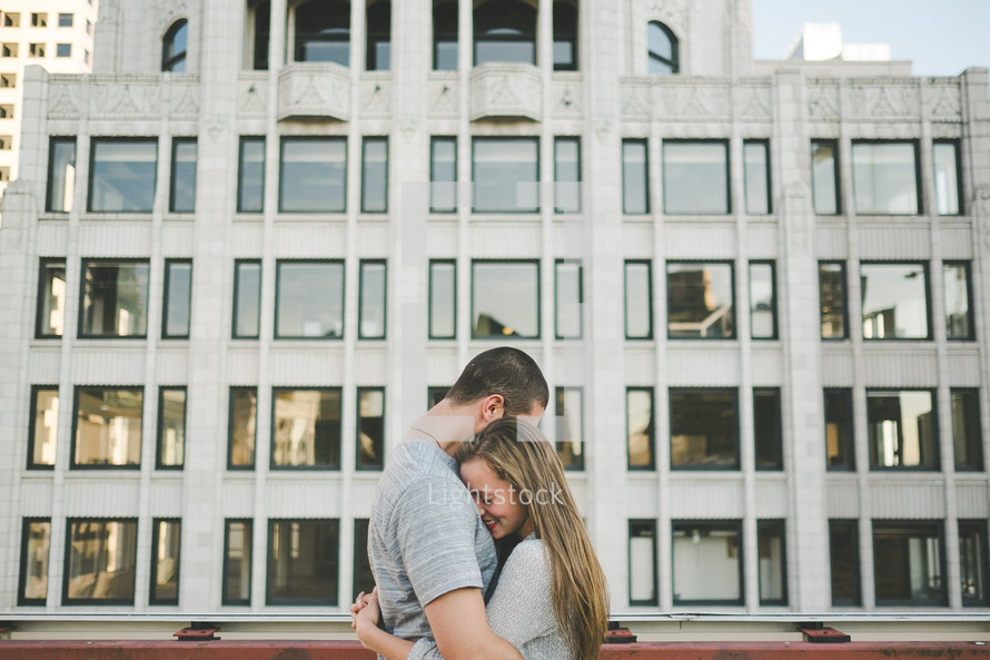 A man and woman hug in front of a large building.