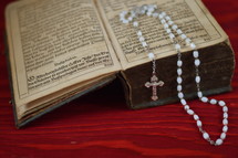 rosary on the pages of  a very old ancient book in old German lettering on red wooden table
