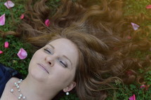 A woman lying in a field of clovers with rose petals 