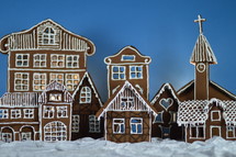 home made gingerbread village in front of blue background on white snowlike velvet as advent decoration