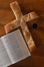 Bread in the shape of a cross with an open bible and a goblet of wine. 
