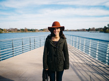 A woman in a red hat stands on a dock over a lake.