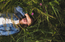 a young woman lying in tall grasses covering her face with her hand 