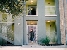 A young woman stands in front of a door at an apartment complex.