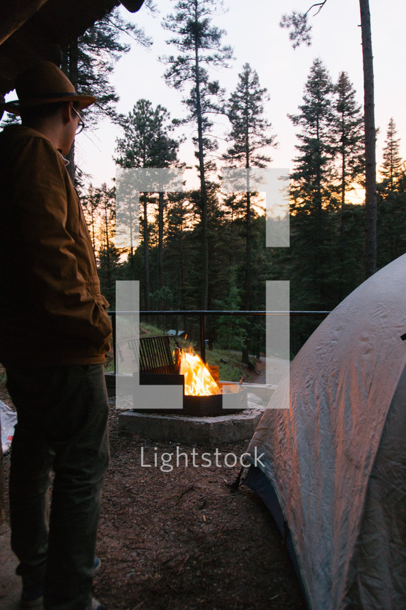 man standing near a tent and campfire 