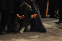 Woman kneeling with arms extended, praising God during worship service.