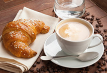 Cappuccino with croissant and glass of water in the tray of brown wood