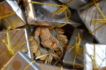 An ornament of baby Jesus in the manger lost among boxes of wrapped gifts.
