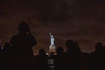 tourists on a ferry photographing the Statue of Liberty at night