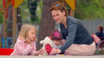 Woman and two children draw with chalk at a park.